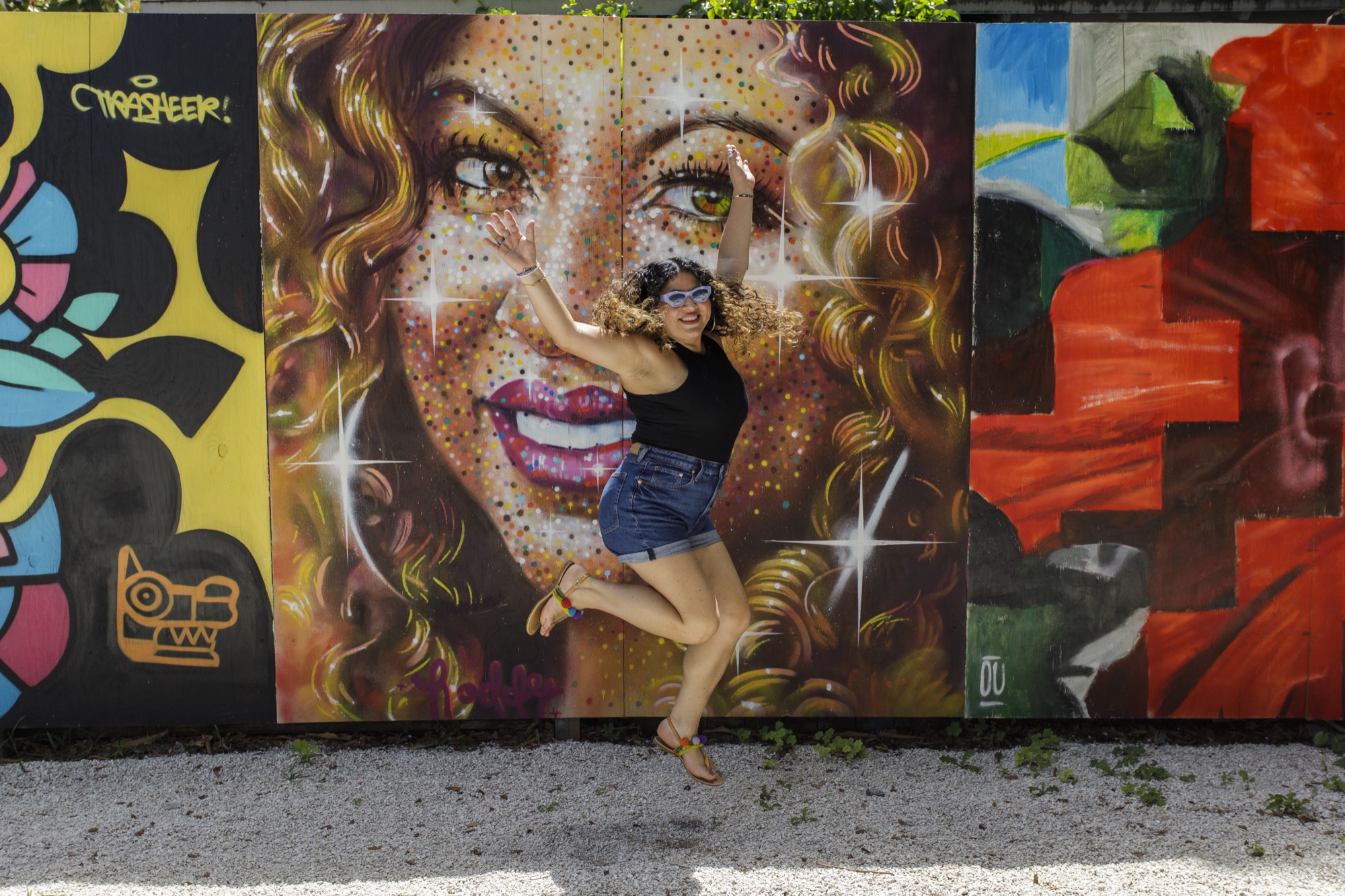 Didi jumping with joy in front of a colorful mural portrait in Little Havana
